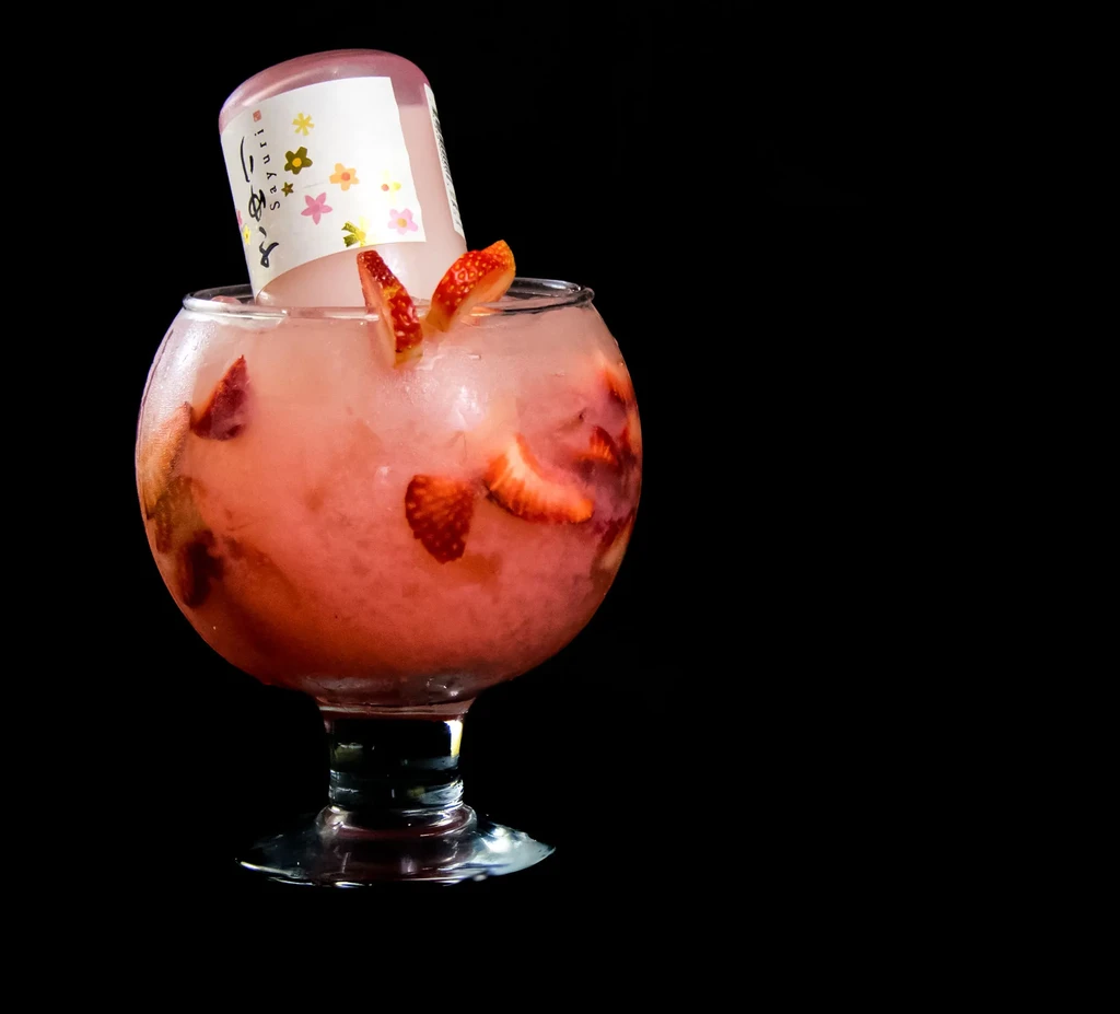 Pink slushy drink with strawberries and an inverted Sayuri sake bottle.