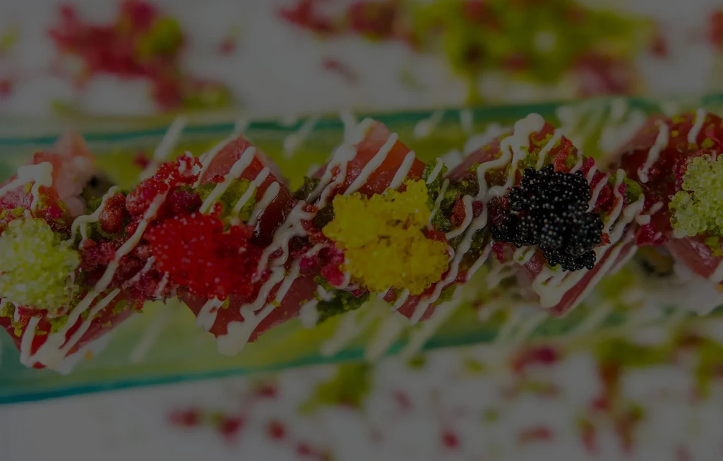 Sushi rolls topped with tuna, colorful roe, and white sauce.