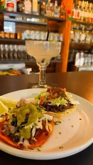 Two vibrant tacos and a salt-rimmed margarita at a bar.