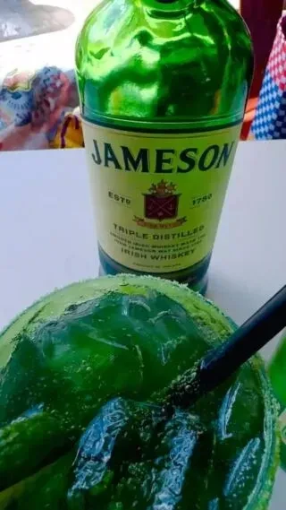 Jameson bottle behind a frothy green cocktail with a sugared rim.