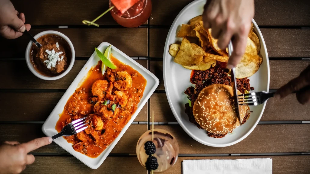 Overhead view of shrimp, burger, beans, chips, and drinks.