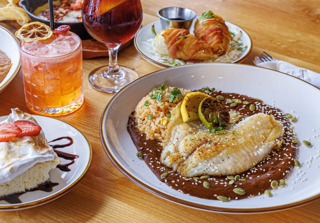Grilled fish, cake, cocktails, and appetizers on a wooden table.