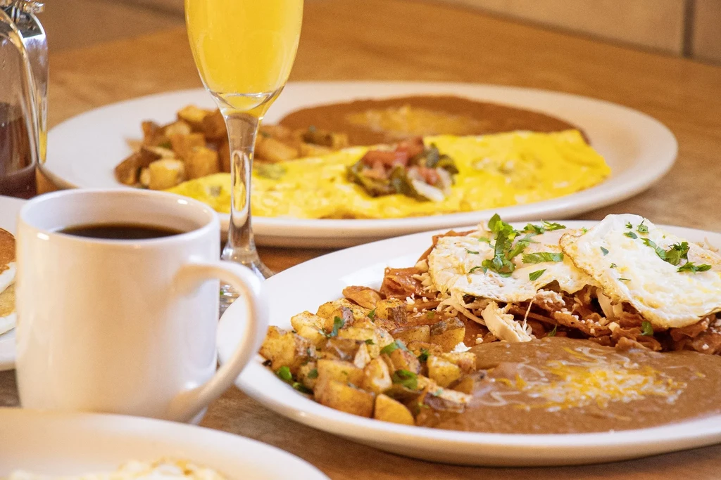 Breakfast dishes: chilaquiles, fried eggs, potatoes, coffee, and orange juice.
