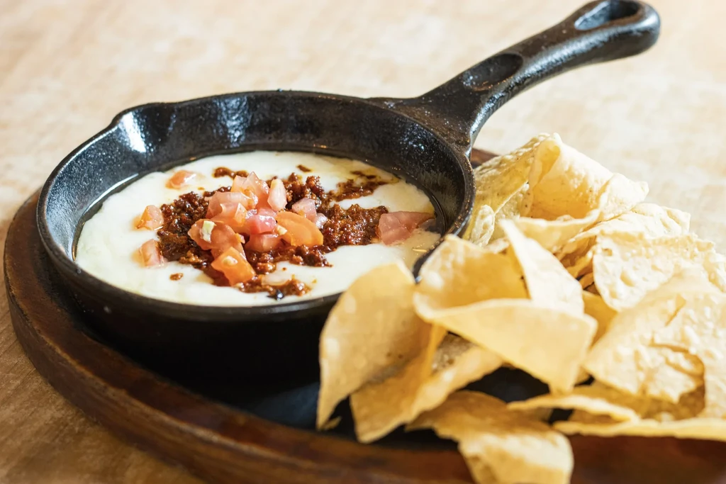 Cast-iron skillet of queso fundido with meat, tomatoes, and tortilla chips.