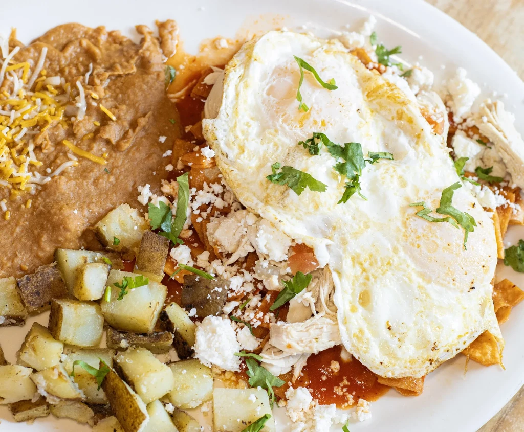 Plate of chilaquiles with fried eggs, refried beans, and roasted potatoes.