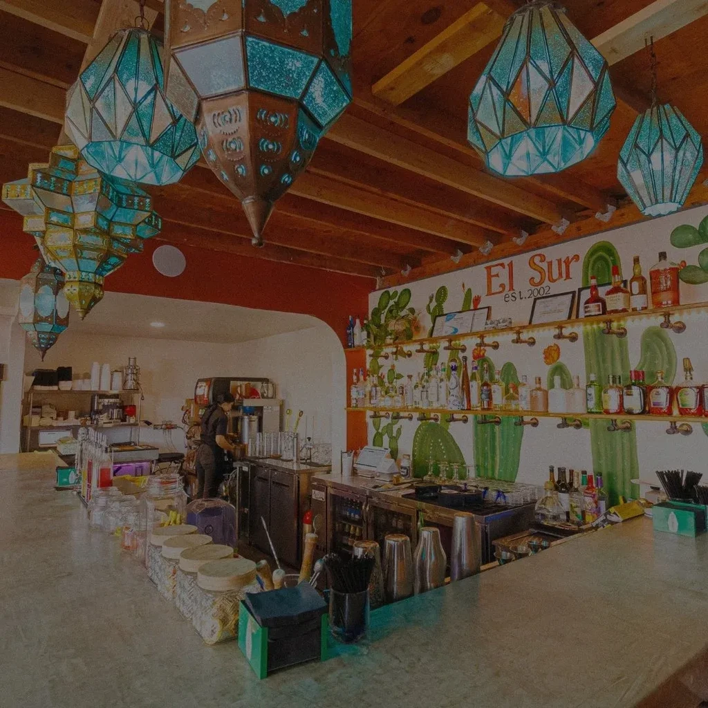 El Sur bar interior: cacti mural, ornate lanterns, and liquor bottles.