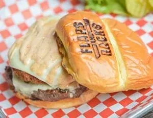 Close-up of a burger with melted cheese and 'FLAPS and RACKS' branded bun.