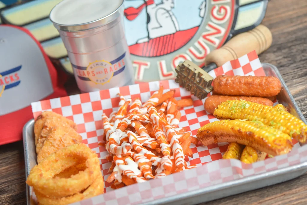 Fried chicken, sweet potato fries, onion rings, and corn on a tray.