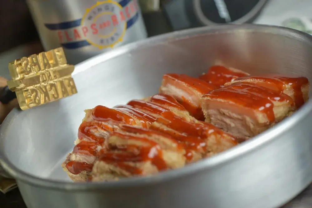 Branded crispy pork belly with red sauce in a metal pan.