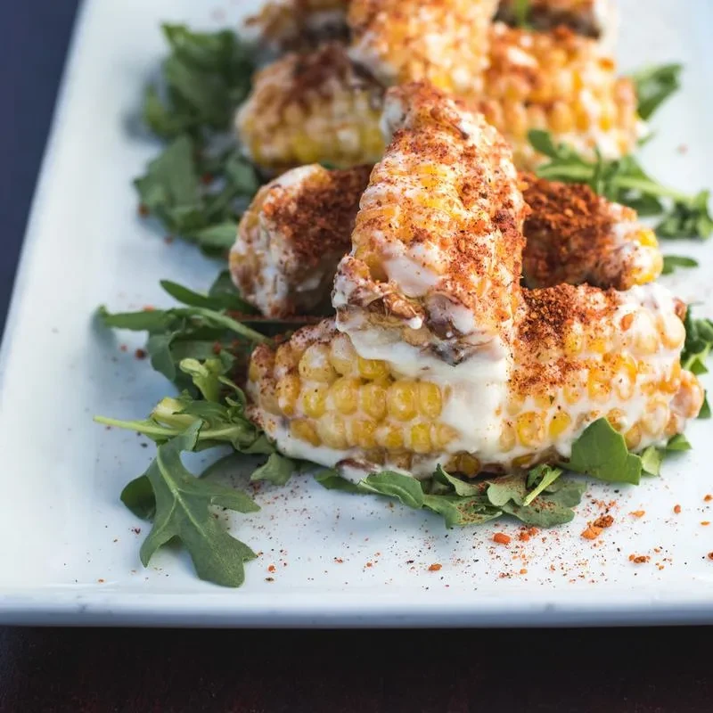 Plate of chili-dusted corn segments with creamy sauce and greens.