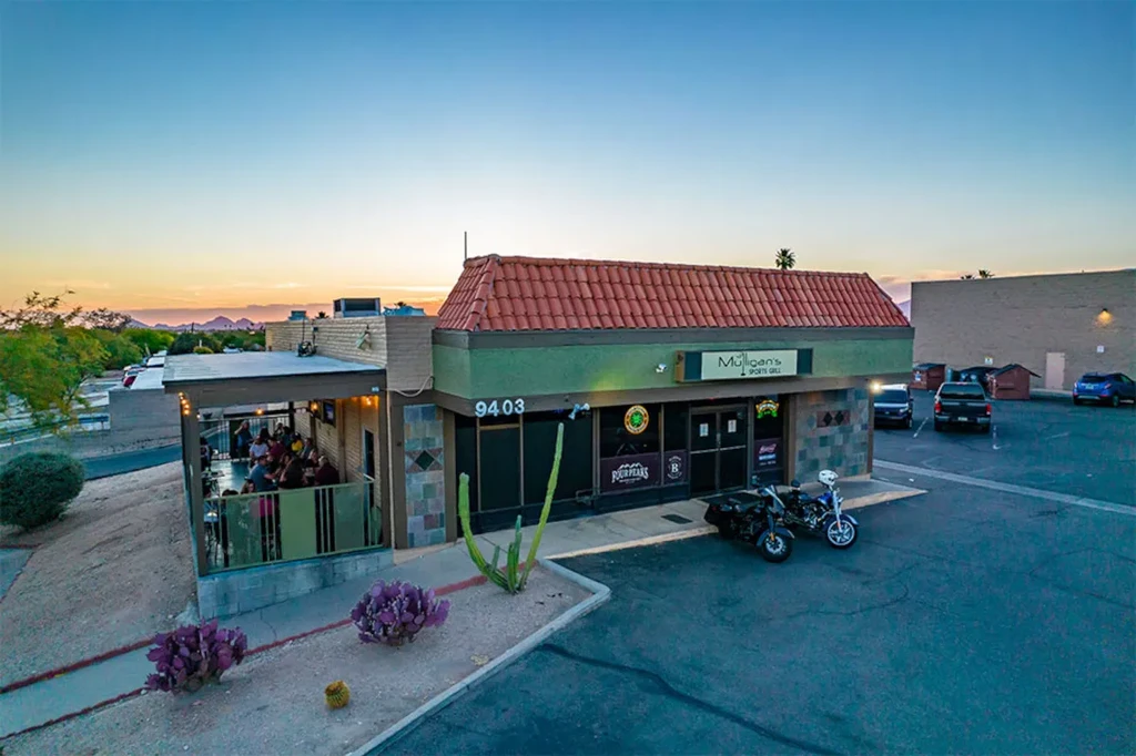 Mulligan's Sports Grill exterior at dusk, patio with people, desert landscape.