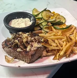 Grilled steak topped with onions, mushrooms, fries, zucchini, and dip.