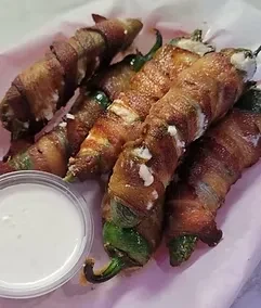 Crispy bacon-wrapped jalapeño poppers with cheese and white dipping sauce.