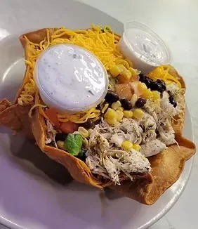Taco salad in crispy tortilla bowl with chicken, cheese, and dressing.