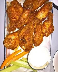 Fried chicken wings, carrots, celery sticks, and white dip on a platter.