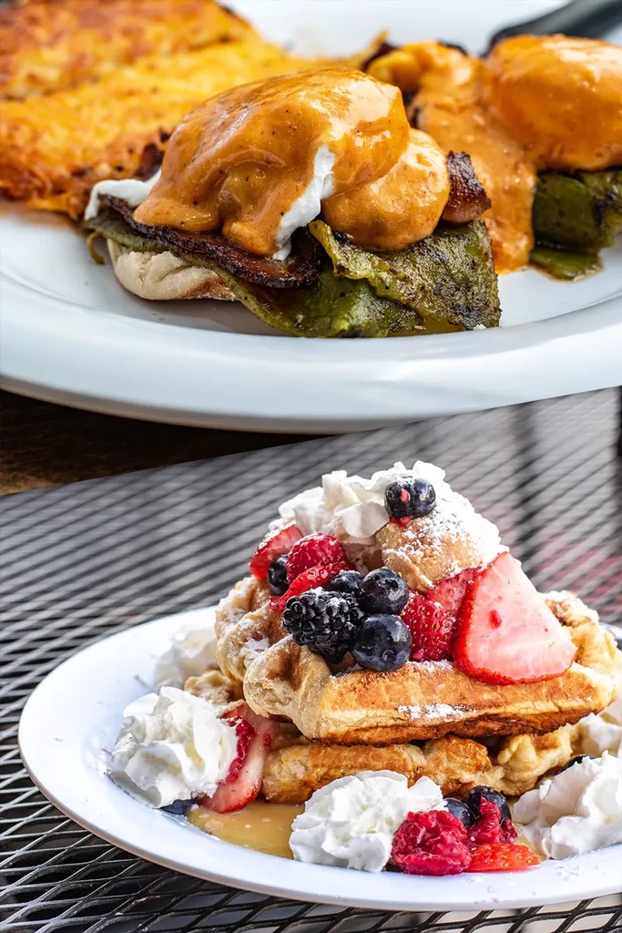 Eggs Benedict with bacon and waffles with mixed berries on plates.