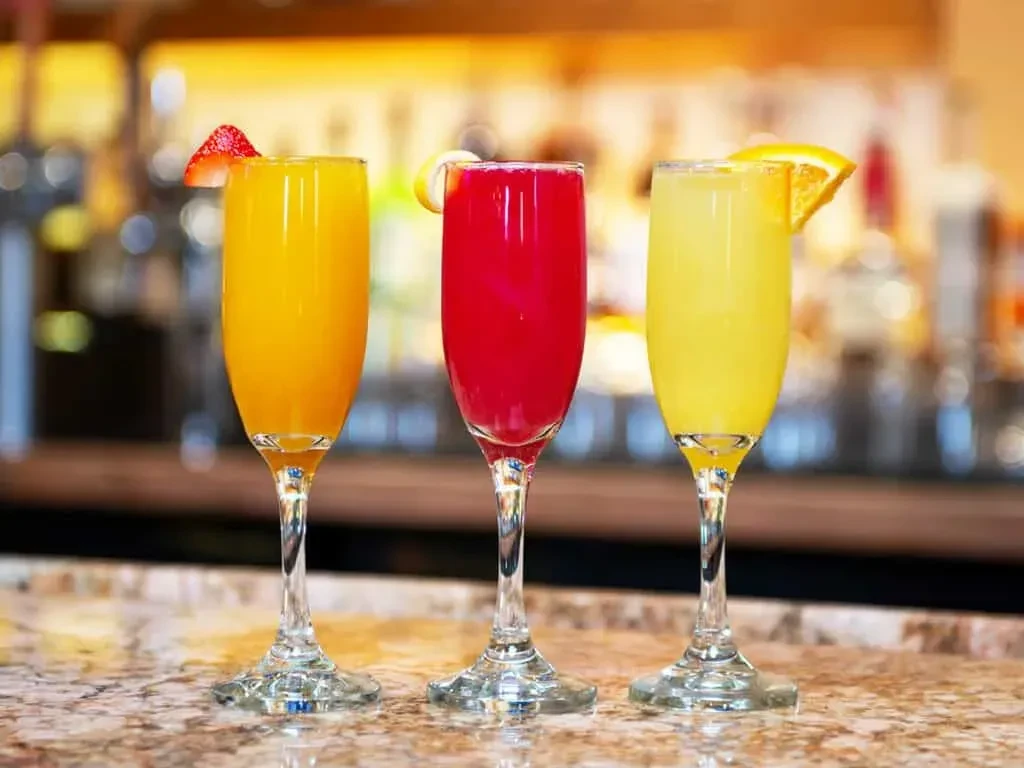 Three colorful, frothy drinks in fluted glasses with garnishes.