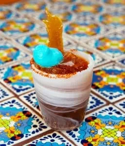 Vibrant cocktail in swirled glass, blue foam, golden garnish, on colorful tiles.