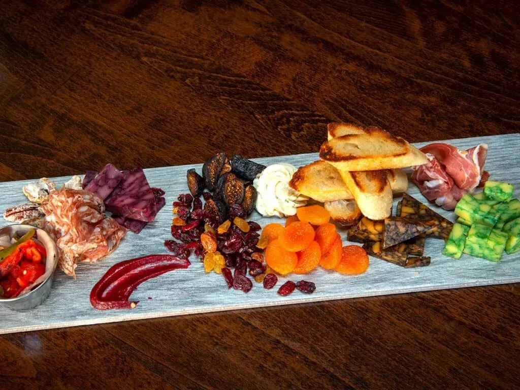 Charcuterie board with colorful cheeses, cured meats, dried fruits, and crostini.
