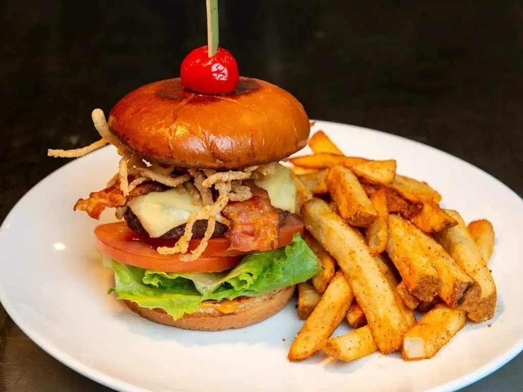 Beef burger with bacon, fried onions, seasoned fries, and cherry skewer.