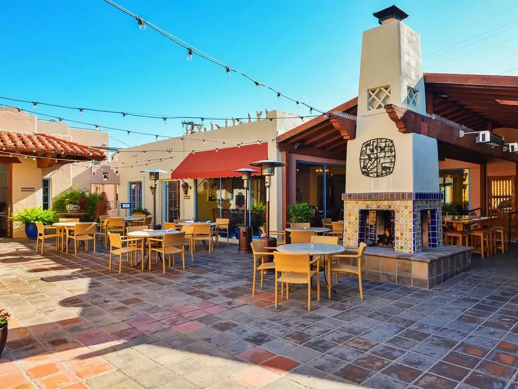 Sunny Spanish-style restaurant patio with tiled fireplace and dining tables.