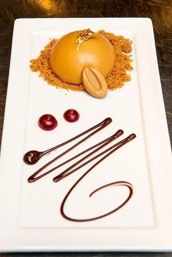 Artfully plated caramel dessert with gold leaf, chocolate, and berry sauces.