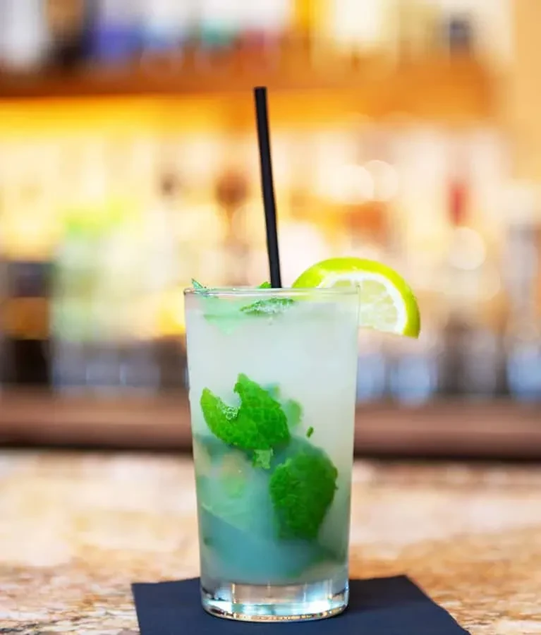 Greenish-white cocktail with mint, lime, black straw, and crushed ice.