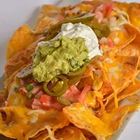 Nachos piled high with melted cheese, guacamole, sour cream, and jalapeños.