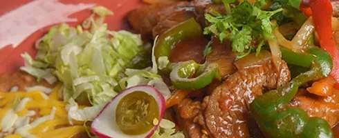 Colorful beef fajitas with lettuce, cheese, radish, and jalapeño garnish.