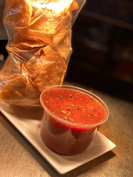 Bag of golden tortilla chips and a cup of chunky red salsa.