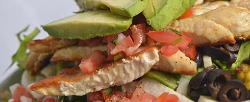 Vibrant stacked salad with grilled chicken, avocado, tomatoes, and olives.