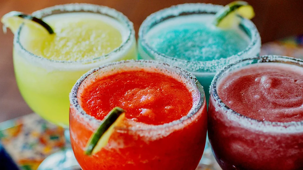 Four vibrant frozen drinks with salt rims and lime wedges.