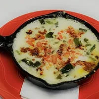 Close-up of melted cheese in cast-iron skillet with green and red toppings.