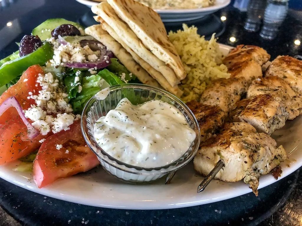 Greek meal with chicken skewers, rice, salad, tzatziki, and pita bread.