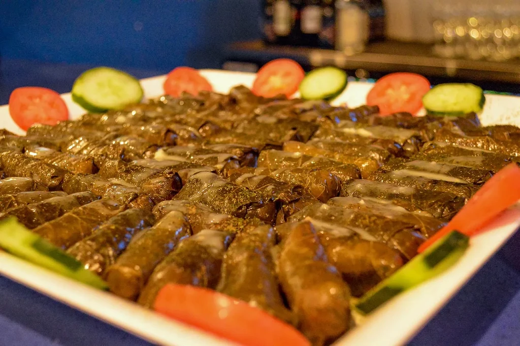 White platter of stuffed grape leaves, garnished with tomato and cucumber.