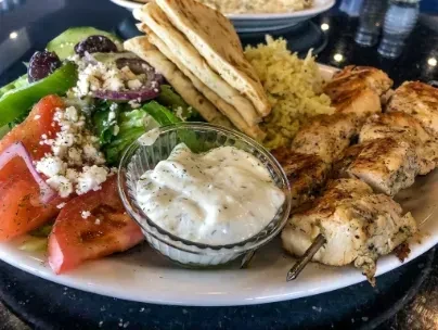 Close-up of Greek grilled chicken skewers, rice, salad, pita, tzatziki.