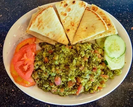 Colorful meal with green dip, pita bread, tomatoes, and cucumbers.
