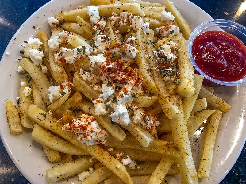 Fries topped with crumbled cheese, paprika, green herbs, and ketchup.
