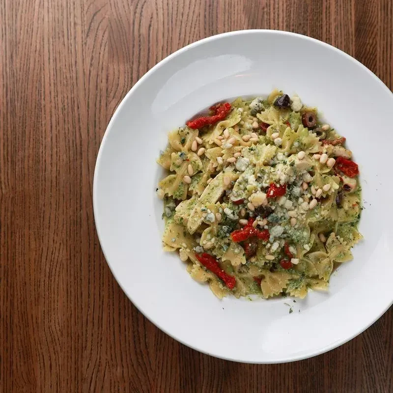Farfalle pasta with pesto, chicken, tomatoes, olives, and cheese.