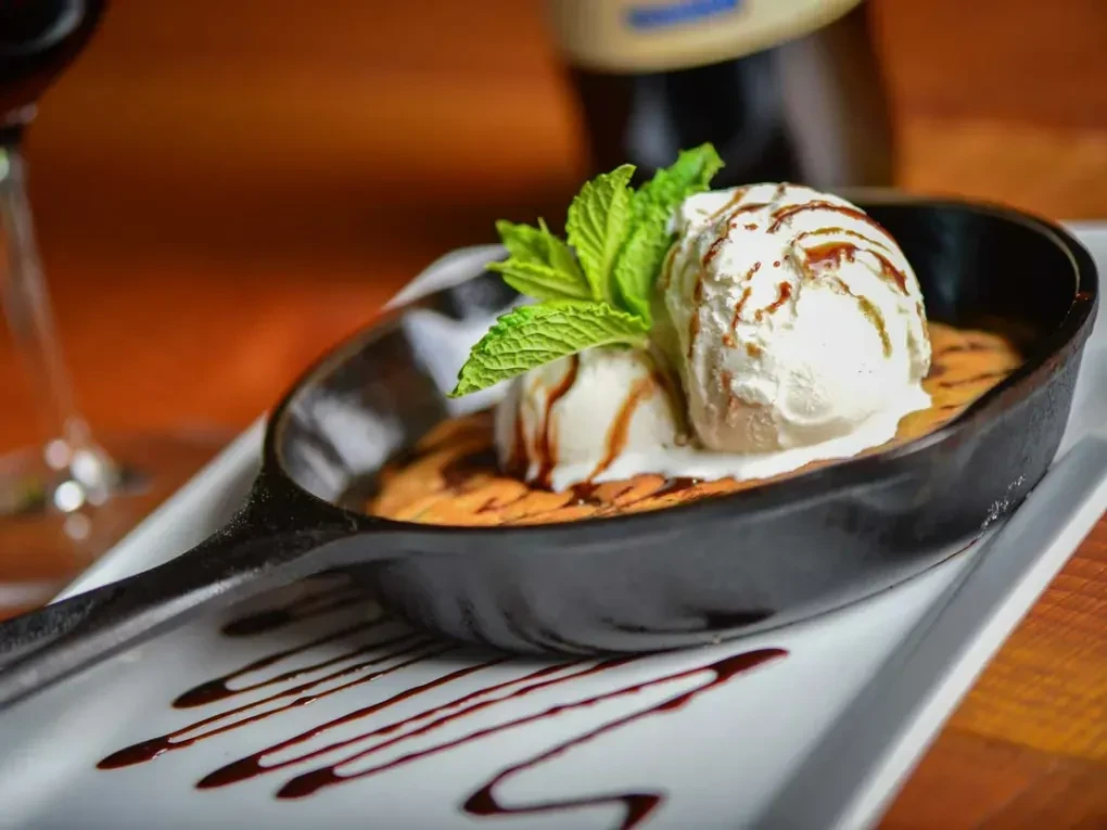Golden-brown cookie skillet with melting vanilla ice cream, dark sauce, and mint.