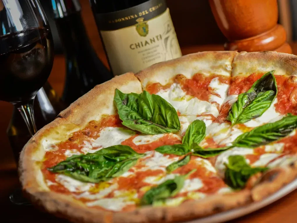 Sliced Margherita pizza with tomato, mozzarella, basil, and red wine.