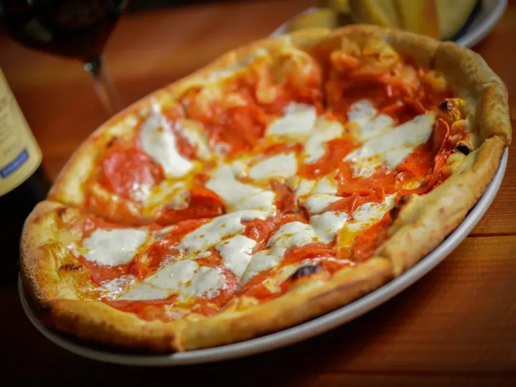 Oval pepperoni pizza with mozzarella, tomato sauce on a wooden table.