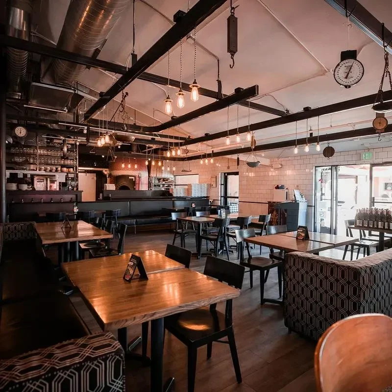 Modern industrial restaurant interior, empty, with pizza oven and bar.