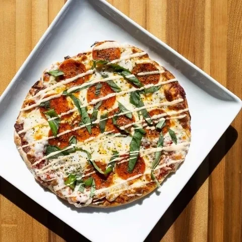 Top-down pepperoni flatbread pizza with basil, drizzled sauce on wood.