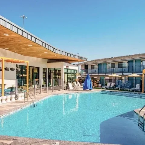 Blue pool, modern building with wood overhang, hotel, lounge chairs.