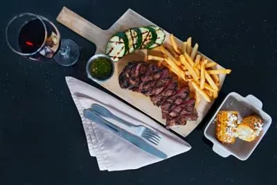 Overhead shot of grilled steak, fries, zucchini, corn, and red wine.