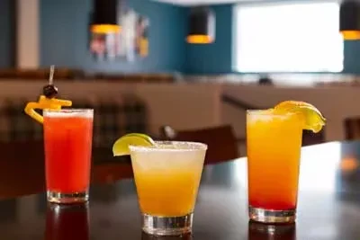 Three vibrant, garnished cocktails on a dark bar surface.