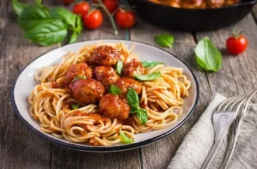 Plate of spaghetti and meatballs with basil on a rustic wood table.