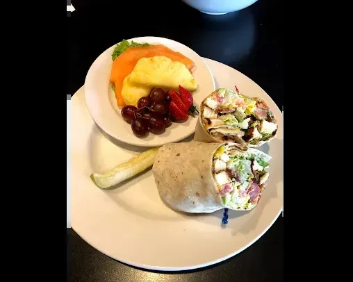 Chicken wrap, pickle spear, and fresh fruit served on white plates.