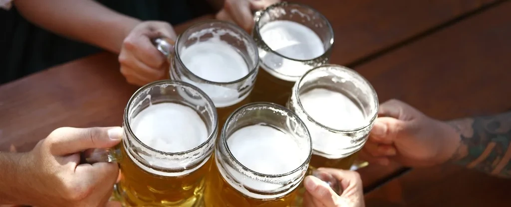 Overhead view: Five foamy beer mugs held by hands, one tattooed.